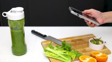 Kadın mutfakta kereviz, elma, mandalina, kivi ve ıspanak karışımından sağlıklı bir içecek hazırlıyor. Spor takım elbiseli kız blender kabında meyve, su ve karışım ekliyor. Kadın ezilmiş meyve, ince vücut 4k.