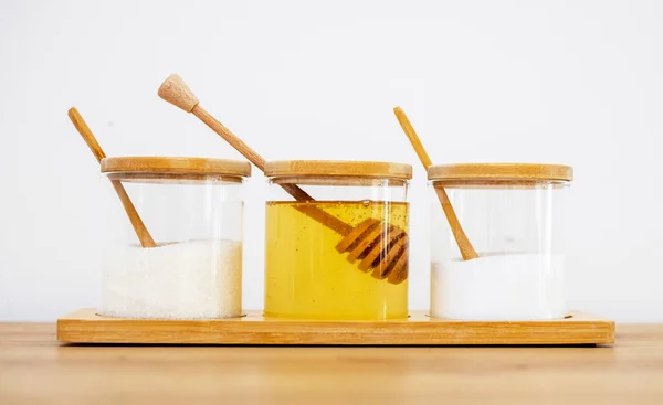 glass jars with salt sugar and honey in. modern kitchen interior,table.wooden spoon honey long stick, round cover, lid. home house design