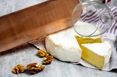 Gül şarabı şişesi, cam, yuvarlak peynir, tek dilim, ceviz, mantar ve tirbuşon karışımı mutfak çizgili havlu ya da gri arka plan taklidi.