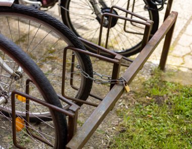 Şehir tarzı sokak fotoğrafının yanındaki otoparkta bir sürü bisiklet var. Tekerlek lastiklerini, bisiklet parçalarını, sepeti, gidonu kapat. Arka arkaya yeşil doğa binaları inşa eden bisiklet.