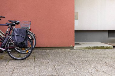 Şehir tarzı sokak fotoğrafının yanındaki otoparkta bir sürü bisiklet var. Tekerlek lastiklerini, bisiklet parçalarını, sepeti, gidonu kapat. Arka arkaya yeşil doğa binaları inşa eden bisiklet.