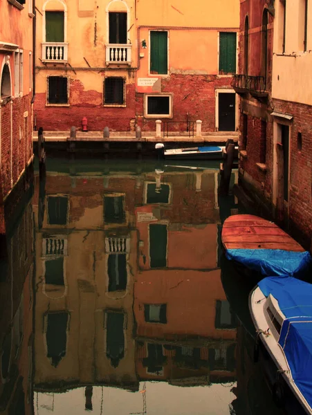 Boats near a vintage brick wall on the water surface of a narrow canal street in Venice, reflections of old houses with windows on a Venetian street. High quality photo