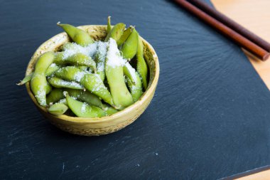 Edamame is a preparation of immature soybeans in the pod, found in cuisines with origins in East Asia. The pods are boiled or steamed and can be served with salt or other seasonings.
