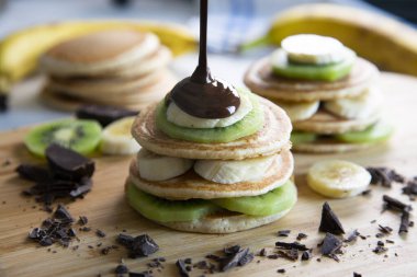 Pancakes with fresh fruit like banana, strawberries or kiwi with a dark chocolate covered.