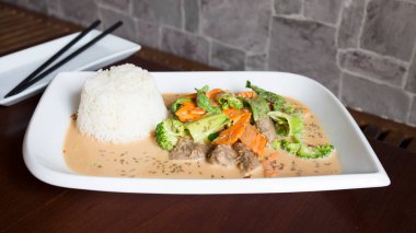 Köri soslu sığır eti ve pirinç ile servis edilen sebzeli Asya tabağı..