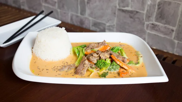 Asian combo plate with beef in curry sauce and vegetables served with rice.