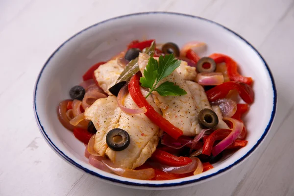 Fish cooked with onion and red pepper and black olives