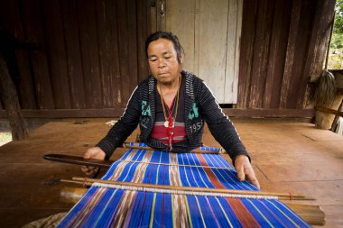 Chiang Rai, Tayland; 1 Ocak 2023: Chiang Rai bölgesindeki yüksek dağların yerli kabilesinden bir kadın el yapımı kumaş örüyor..