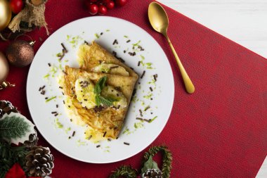 Limon suyuyla marine edilmiş muz parçalarıyla dolu krep Noel süsleme elementleriyle dolu bir masada..