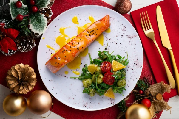 Grilled salmon with orange sauce and a salad. Typical Mediterranean coast dish. Christmas food served on a table decorated with Christmas motifs.