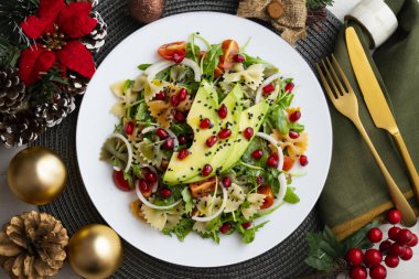 Makarna yayları, avokado, kiraz domatesleri, nar ve susamlı argula salatası Noel motifleriyle süslenmiş bir masada servis edilir..