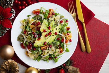Makarna yayları, avokado, kiraz domatesleri, nar ve susamlı argula salatası Noel motifleriyle süslenmiş bir masada servis edilir..