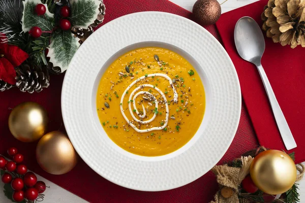 Carrot and pumpkin cream with cream and nuts. Christmas food served on a table decorated with Christmas motifs.