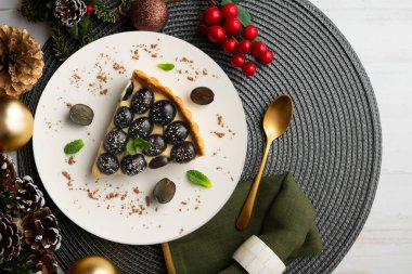 Lezzetli siyah üzümlü pasta, üzerinde pasta kreması ve Noel süslemeleri olan bir masa..