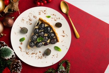 Lezzetli siyah üzümlü pasta, üzerinde pasta kreması ve Noel süslemeleri olan bir masa..