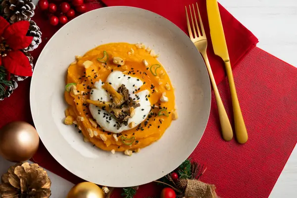 stock image Sweet potato cream with poached egg and mushrooms. Plate on a table with Christmas decoration.