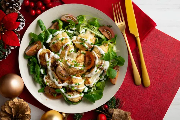 Kızarmış karnabahar salatası ve sebze ve yoğurt sosu. Noel süslemeli bir masada yemek.