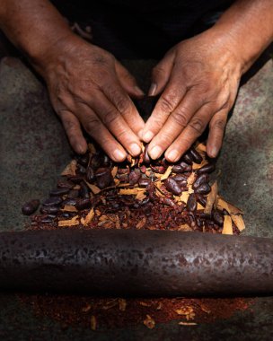 A woman in Oaxaca Mexico manually producing organic chocolate on a metate, an ancient stone tool for grinding food products. clipart