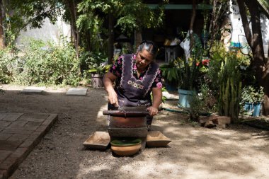 Teotitlan del valle, Oaxaca, Meksika; 1 Kasım 2024: Geleneksel bir aşçı, malzemeleri öğütmek için antik bir mutfak gereci olan metaya çikolata öğüttü.