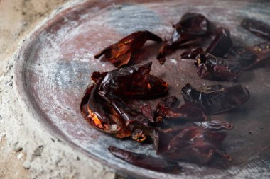 Preparing Mexican Mole Negro. Oaxaca chiles have to be cleaned, toasted on a comal over a flame and soaked in water before grinding with metate. clipart