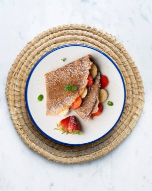 Çilek ve taze muzla dolu çikolatalı krepler. Noel süslemeleri ile en üstteki görünüm masası.