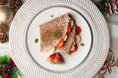 Çilek ve taze muzla dolu çikolatalı krepler. Noel süslemeleri ile en üstteki görünüm masası.