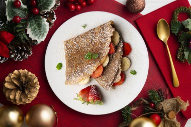 Çilek ve taze muzla dolu çikolatalı krepler. Noel süslemeleri ile en üstteki görünüm masası.