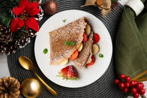 Çilek ve taze muzla dolu çikolatalı krepler. Noel süslemeleri ile en üstteki görünüm masası.