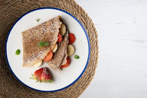Çilek ve taze muzla dolu çikolatalı krepler. Noel süslemeleri ile en üstteki görünüm masası.