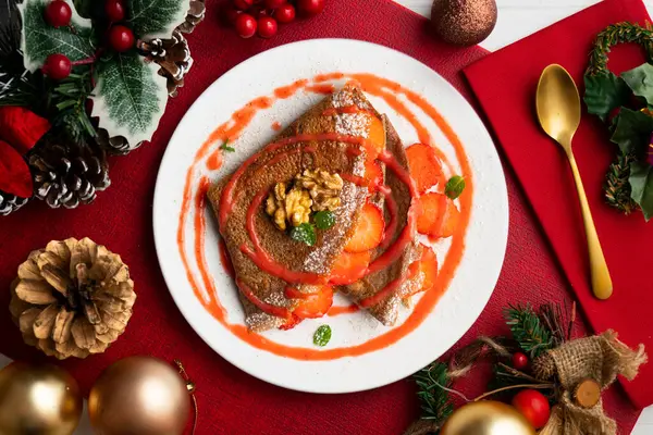 Çilek ve meyve sosuyla dolu çikolatalı krepler. Noel süslemeleri ile en üstteki görünüm masası.