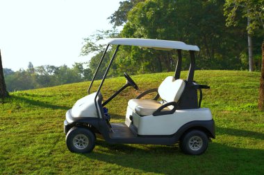 Golf sahasına park etmiş sabah güneşli beyaz golf arabası.