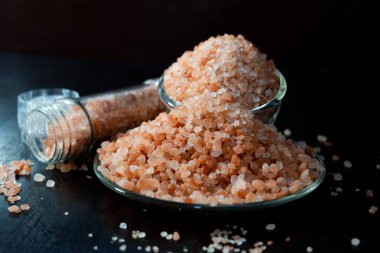 Himalaya tuzu temiz kavanozda ve siyah ahşap masaya yerleştirilmiş tabakta..
