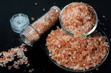 Himalaya tuzu temiz kavanozda ve siyah ahşap masaya yerleştirilmiş tabakta..