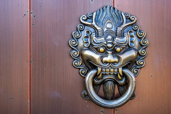 Metal dragon head door knocker in front of the entrance of Chinese temple, art related to religious beliefs.