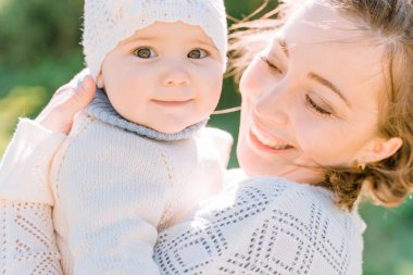 A young woman holds her one year old daughter in her arms while walking in the village, they look and smile