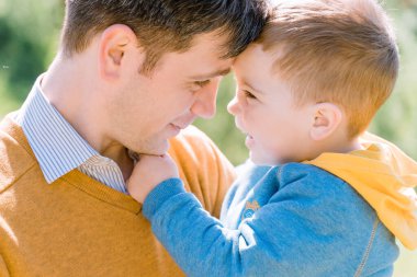 Üç yıldır gülümseyen sevimli bir çocuk yetişkin, siyah ve beyaz bir çocuğun bacaklarının arkasında saklanıyor.