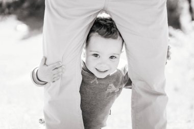 Üç yıldır gülümseyen sevimli bir çocuk yetişkin, siyah ve beyaz bir çocuğun bacaklarının arkasında saklanıyor.