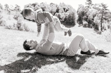 Genç baba çimenlerin üzerinde yatıyor. Üç yıldır kollarında gülümseyen bir oğul, aktif ebeveynlik kavramı, temiz havada ortak oyunlar ve uyumlu eğitim.