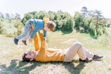 Young father lies on the grass he fools around with his smiling son of 3 years in his arms, the concept of active parenthood, joint games in the fresh air and harmonious education