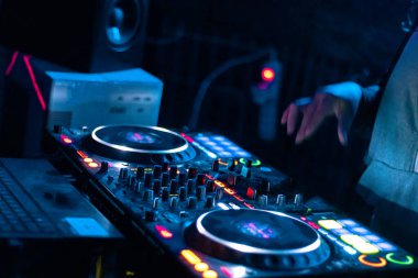 Elektronik bir partide çalan DJ 'in elleri. Renkli ışıklar ve konsolda karışık müzik.