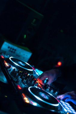 Elektronik bir partide çalan DJ 'in elleri. Renkli ışıklar ve konsolda karışık müzik.
