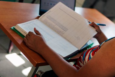 Okulda bilgisayarında çalışan esmer Latin 'in elleri görünüyor. Dizüstü bilgisayarında yazı yazıp, bir sınıfta kitap yazıyor..