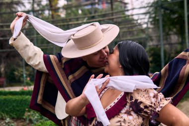 Şilili huasolar gibi giyinmiş, romantik poz veren ve geleneksel bir Şili dansı olan Cueca 'yı öpüp dans eden genç bir çiftin portresi. Şili gelenekleri, kutlamalar ve kültür.                          