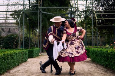 Şilili huasolar gibi giyinmiş, romantik poz veren ve geleneksel bir Şili dansı olan Cueca 'yı öpüp dans eden genç bir çiftin portresi. Şili gelenekleri, kutlamalar ve kültür.                          