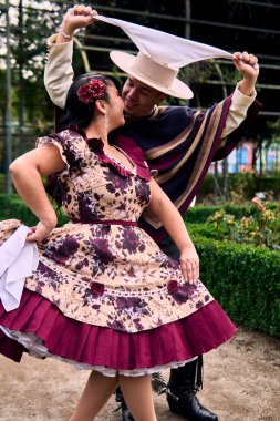 Şilili huasolar gibi giyinmiş, romantik poz veren ve geleneksel bir Şili dansı olan Cueca 'yı öpüp dans eden genç bir çiftin portresi. Şili gelenekleri, kutlamalar ve kültür.                          