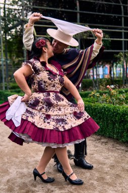 Şilili huasolar gibi giyinmiş, romantik poz veren ve geleneksel bir Şili dansı olan Cueca 'yı öpüp dans eden genç bir çiftin portresi. Şili gelenekleri, kutlamalar ve kültür.                          