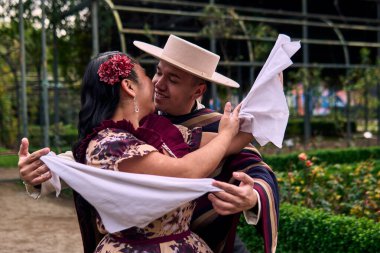 Şilili huasolar gibi giyinmiş, romantik poz veren ve geleneksel bir Şili dansı olan Cueca 'yı öpüp dans eden genç bir çiftin portresi. Şili gelenekleri, kutlamalar ve kültür.                          