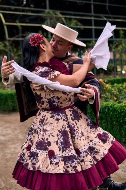 Şilili huasolar gibi giyinmiş, romantik poz veren ve geleneksel bir Şili dansı olan Cueca 'yı öpüp dans eden genç bir çiftin portresi. Şili gelenekleri, kutlamalar ve kültür.                          