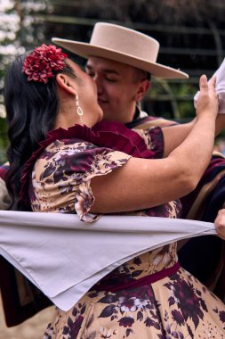 Şilili huasolar gibi giyinmiş, romantik poz veren ve geleneksel bir Şili dansı olan Cueca 'yı öpüp dans eden genç bir çiftin portresi. Şili gelenekleri, kutlamalar ve kültür.                          