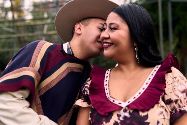 Şilili huasolar gibi giyinmiş, romantik poz veren ve geleneksel bir Şili dansı olan Cueca 'yı öpüp dans eden genç bir çiftin portresi. Şili gelenekleri, kutlamalar ve kültür.                          